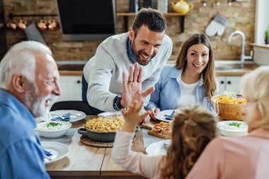 Happy man having fun while giving high-five to his daughter while having family lunch at home. 