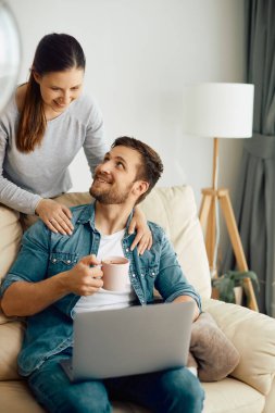 Happy couple talking while surfing the net on laptop at home.