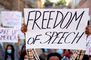 Close-up of black man protesting with large group of people and holding a placard with freedom of speech inscription. 