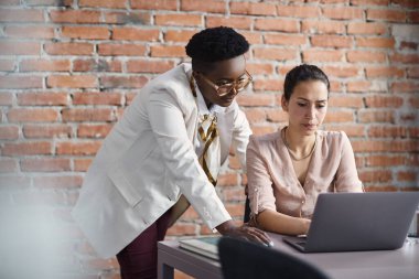 African American businesswoman and her female colleague reading an e-mail on a computer while working at corporate office.
