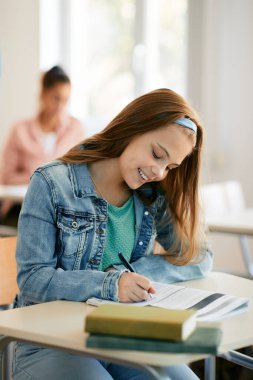 Happy high school student writing in notebook during lecture in the classroom.