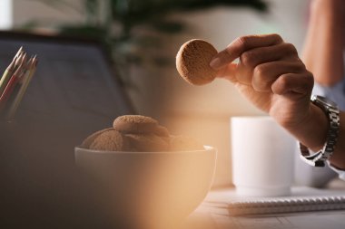 Close-up of businesswoman having cookie as a snack while working in the office. 