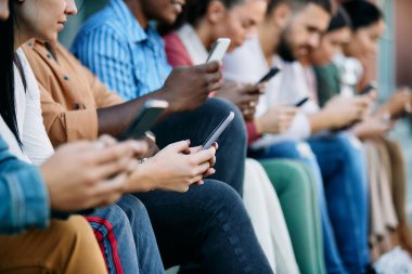 Close-up of female student and her university friends texting on mobile phone at campus. 