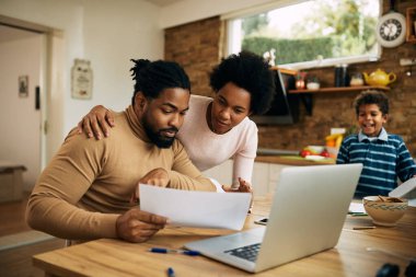 Black couple going through paperwork while working at home. Their son is in the background. 