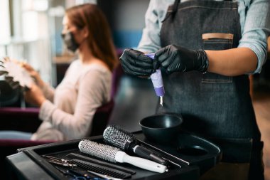 Close-up of hairdresser squeezing hair color from tube at hair salon.