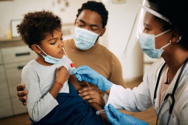 African American doctor using cotton swab while PCR testing small boy at medical clinic. 