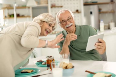 Happy senior couple making video call over touchpad while having breakfast at home. 