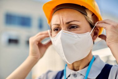 Female engineer protecting herself with face mask while working at construction site during COVID-19 pandemic. 