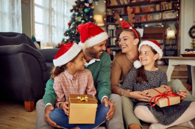 Happy little girls holding presents and having fun with their parents on Christmas day at home. 