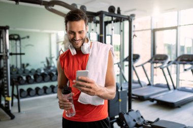 Young happy athlete using smart phone an reading text message in a gym. 