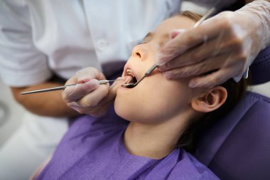 Close-up of small girl having her teeth checked by dentist at dental clinic. 