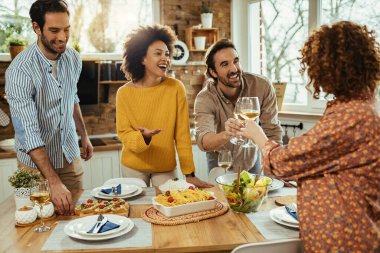 Group of happy friends having fun while preparing dining table for lunch and toasting with wine.