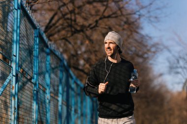 Young happy runner carrying bottle of water while jogging outdoors. 