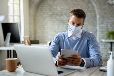 Businessman wearing protective face mask while using touchpad and working in the office. 