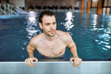 Pensive man relaxing in the swimming pool while spending a day at health spa. 