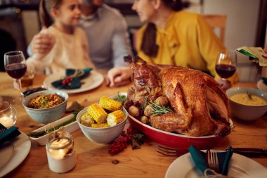 Close-up of Thanksgiving turkey on dining table with family in the background.