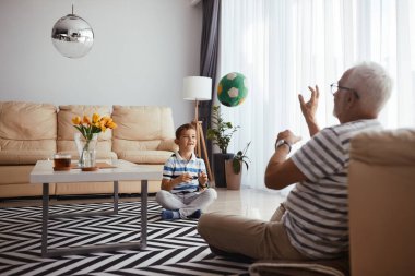 Happy grandfather and grandson having fun and playing with ball at home. Focus is on boy. 