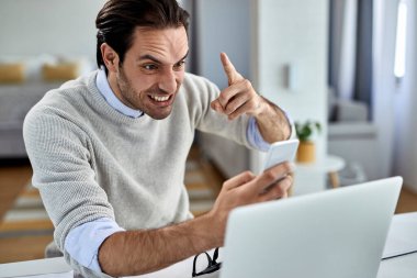 Angry entrepreneur text messaging on cell phone while working at home.