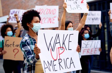 Black female activist holding 'wake up America' sign during anti-coronavirus protest.