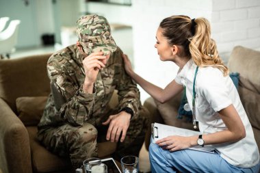 Female doctor comforting sad military man while visiting him at home. 