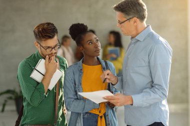 African American college students and her friend talking with their teacher while standing in a lobby.  