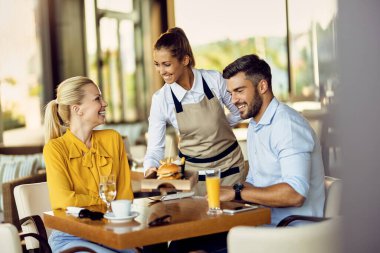 Happy couple enjoying in a restaurant while the waitress is serving them food. Focus is on waitress. Copy space.  