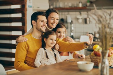 Happy parents with two daughters taking selfie with smart phone at home. 