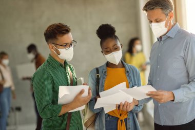 Two students and their teacher wearing face masks while having consultations at university hallway. 