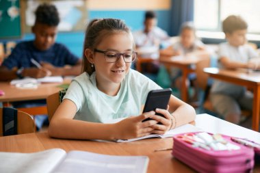 Happy schoolgirl using mobile phone during a class in the classroom. 