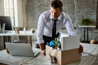 Sad entrepreneur packing his belongings in cardboard box while leaving the office after losing his job. 