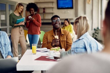 African American university student laughing while communicating with female colleague on lunch break in cafeteria. 