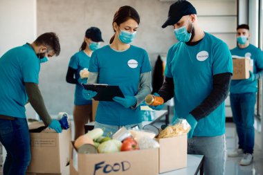 Volunteers wearing face masks while working in charitable foundation and packing donation boxes for food bank. 
