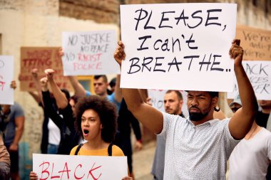 Young black man holding I can't breathe placard while marching with group of protesters against police brutality. 