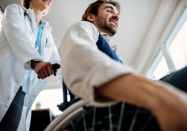 Doktorun tekerlekli sandalyedeki engelli adamı itme görüntüsü düşük açılı. 