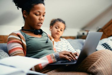 African American woman working on a computer while being with her daughter at home.