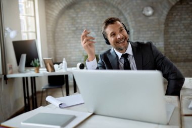 Happy entrepreneur with headset using computer while having video conference in the office.