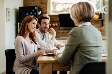 Happy woman signing a document while being with her husband on a meeting with insurance agent. 