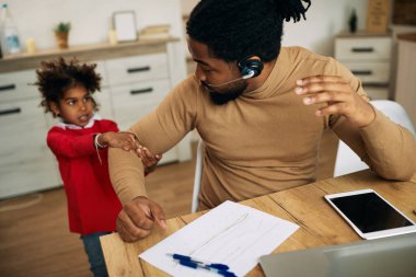 African American single father working at home while daughter is pulling his arm and demanding his attention. 