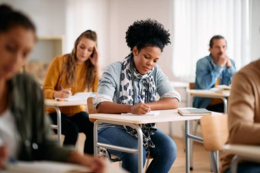 Mid adult black student writng in her notebook while studying at lecture hall.