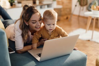 Happy mother and her cute little son surfing the net on a computer at home. 