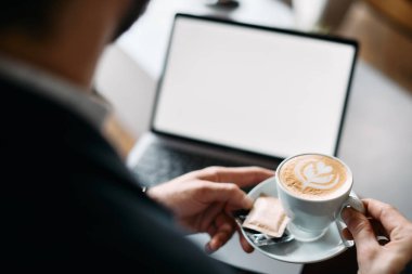 Close-up of businessman drinking coffee while working on a computer in cafe.