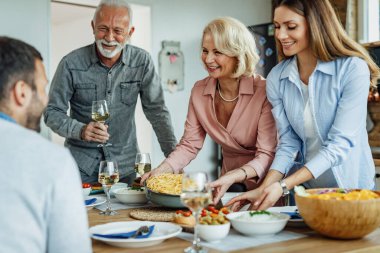 Happy family talking while making preparations for a family lunch at home. Focus is on senior woman. 
