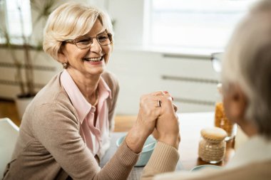 Mutlu olgun bir kadın, kahvaltıda kocasıyla el ele tutuşurken kocasıyla konuşuyor.. 