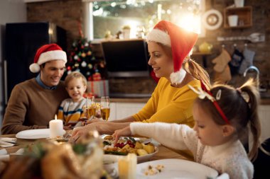 Happy parents and their kids eating lunch at dining table on Christmas day. Focus is on woman. 