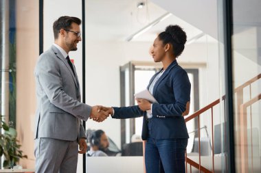 Happy African American businesswoman greeting her colleague in a hallway of an office building. 