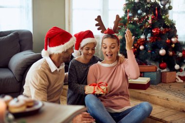 Excited woman getting Christmas present from her daughter and son at home.