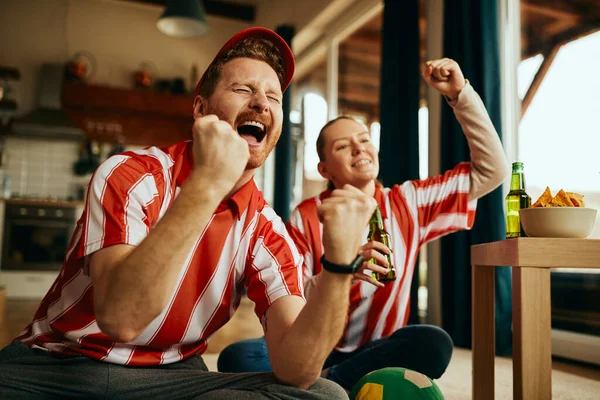 Cheerful sport fans celebrating victory of their team while watching match on TV at home.