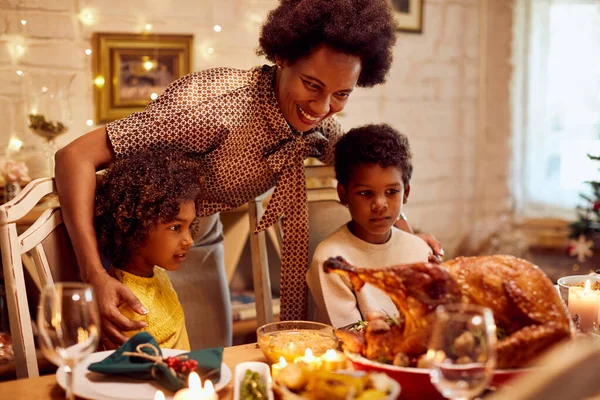 Happy black mother with two son and daughter celebrating Thanksgiving and gathering at dining table at home.