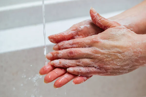 Close-up of woman cleaning hands with soap in the bathroom.