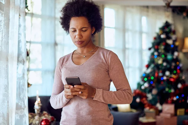 Pensive black woman resting text message on smart phone on Christmas at home.